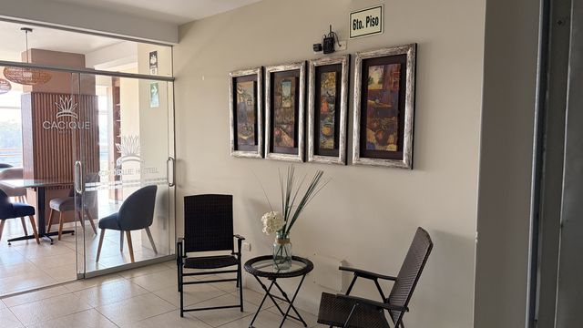 Área común del Cacique Hotel con butacas y cuadros junto al pasillo
